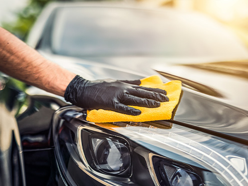 a imagem ilustra uma mão segurando um pano enquanto passa em um carro preto