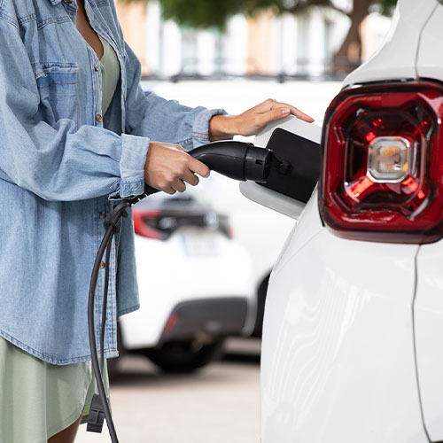 Imagem mostra uma mulher carregando o carro elétrico.