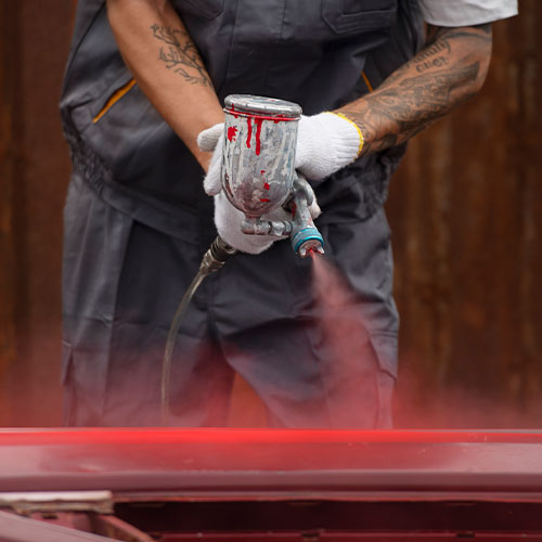 Imagem ilustra um homem pintando uma lataria na cor vermelha.