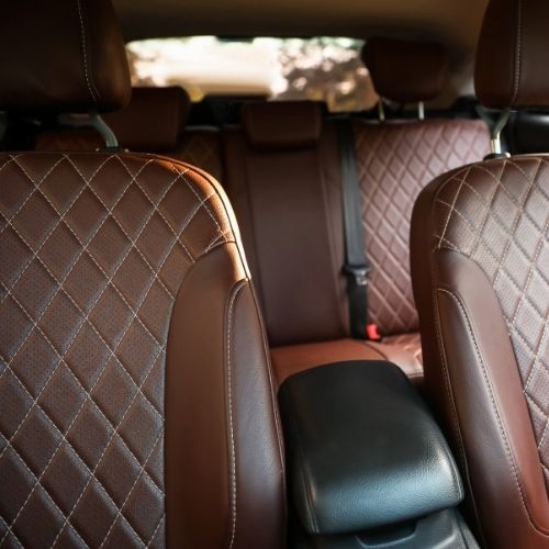 A imagem mostra o interior de um carro com bancos de couro marrom com detalhes.
